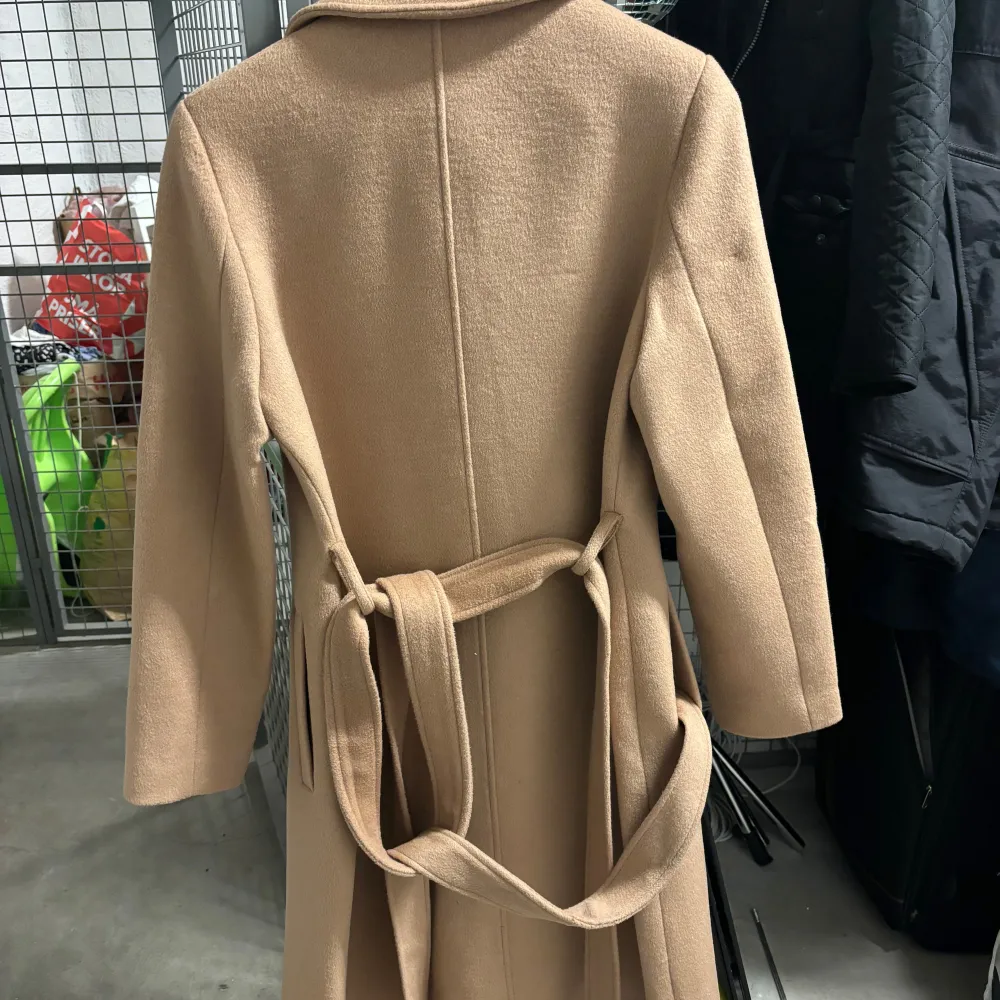 Säljer en superfin beige kappa från Hollies i storlek 36. Den är långärmad och har en klassisk design med knappar framtill. Perfekt för höst och vår, och den har ett bälte i midjan för en snygg passform. Materialet känns lyxigt och håller dig varm under kyliga dagar.. Takit.