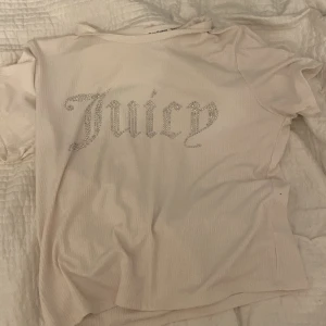 Vit t-shirt från Juicy Couture - Säljer en vit t-shirt från Juicy Couture med glittrande text på framsidan. T-shirten är kortärmad och har en ribbad struktur. Perfekt för en avslappnad och stilren look! Aldrig använd!