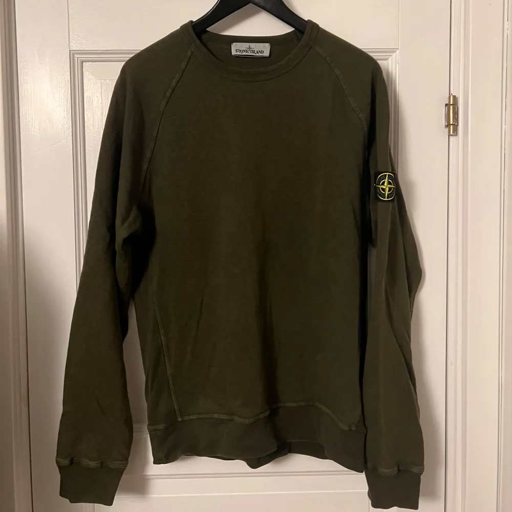 Säljer en snygg olivgrön tröja från Stone Island. Den har en klassisk rund hals och långa ärmar. På ärmen finns det ikoniska Stone Island-märket. Perfekt för en stilren och avslappnad look!. Tröjor & Koftor.