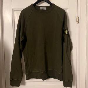 Säljer en snygg olivgrön tröja från Stone Island. Den har en klassisk rund hals och långa ärmar. På ärmen finns det ikoniska Stone Island-märket. Perfekt för en stilren och avslappnad look!