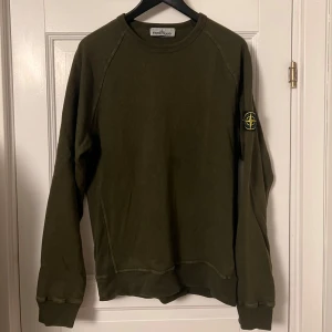 Olivgrön tröja från Stone Island - Säljer en snygg olivgrön tröja från Stone Island. Den har en klassisk rund hals och långa ärmar. På ärmen finns det ikoniska Stone Island-märket. Perfekt för en stilren och avslappnad look!