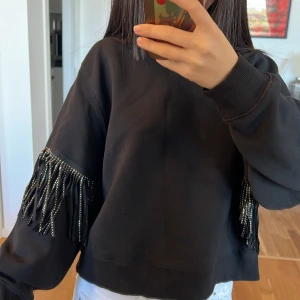 Svart tröja med fransdetaljer Zara 💞 - Säljer en supercool svart tröja med fransdetaljer på ärmarna. Den är perfekt för att ge lite edge till din outfit. Tröjan har en loose passform och är gjord i ett mjukt material som är skönt att ha på sig. Perfekt för höst och vinter!💓