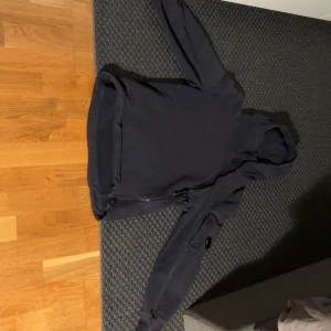 Svart hoodie från C.P. Company - Säljer en svart hoodie från C.P. Company. Den har en enkel design med en huva och långa ärmar. Perfekt för en casual look. Det finns en liten skada på tyget syns knappt , men annars i bra skick.