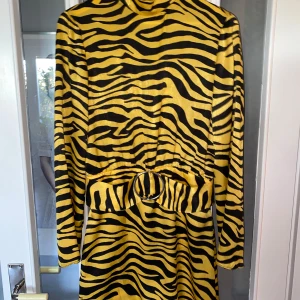 Zebramönstrad klänning med bälte - Säljer en supercool zebramönstrad klänning i gult och svart. Den har långa ärmar och en snygg öppen ryggdetalj. Klänningen kommer med ett matchande bälte som ger en fin passform. Perfekt för en fest eller en utekväll!