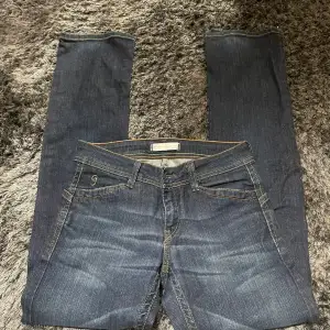 Säljer ett par snygga blå jeans från G-Star i storlek 150/26. De har en klassisk femficksdesign med coola sömmar på bakfickorna. Jeansen är i regular fit och passar perfekt för vardagsbruk. De är i bra skick och redo för en ny ägare!