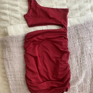 Vinröd oneshoulder klänning - Snygg vinröd oneshoulder klänning i ett mjukt och stretchigt material. Perfekt för festliga tillfällen med sin eleganta och moderna design. Klänningen har en åtsittande passform som framhäver figuren.