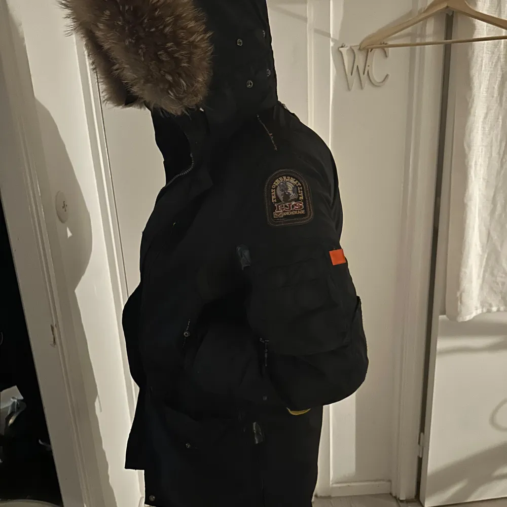 Säljer en svart parkajacka från Parajumpers i storlek M. Jackan har en mysig pälsfodrad huva och praktiska fickor. Perfekt för kalla vinterdagar med sin varma och skyddande design. Den har en dragkedja och knappar för extra skydd mot kyla. Passar både till vardags och mer äventyrliga utflykter.. Jackor.