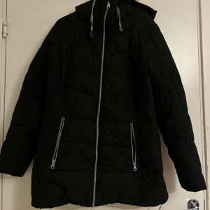 Svart pufferjacka från North Bend - Säljer en svart pufferjacka från North Bend i storlek 40. Jackan har en dragkedja framtill och två praktiska fickor med dragkedjor. Perfekt för kalla dagar med sin varma och vadderade design. Den har en hög krage och en huva för extra skydd mot väder och vind.