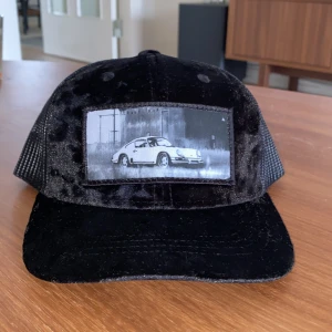 Svart keps med bilmotiv - Snygg svart keps med tryck av en klassisk bil. Kepsen har en mesh-baksida och är justerbar. Passar de flesta tack vare one size-designen. Är helt ny, säljer  pga att den var för stor.