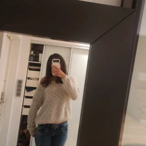 Beige stickad tröja från Lely Owood - Mysig beige stickad tröja från Lely and wood i storlek S/M. Perfekt för höst och vinter med sin varma och bekväma design. Tröjan har en söt svart rosett i nacken och långa ärmar.