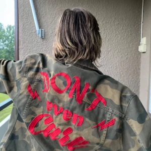  jeansjacka i militärprint   - Supersnygg och oversized jeansjacka i militärprint och med röd text på ryggen! Den är i storlek L och har flera fickor 💕