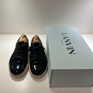 Lanvin Sneakers - Säljer ett par stilrena svarta sneakers från Lanvin i nyskick. De har en snygg glansig finish och klassisk snörning. Perfekta för både vardag och fest! Kommer med originalkartong och dustbag. Storlek 42 men passar upp till Storlek 43. 