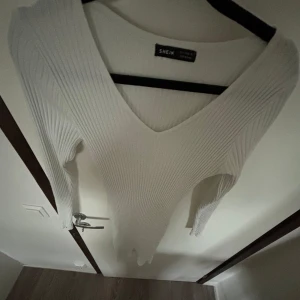 Vit ribbad klänning från Shein - Säljer en stilren vit ribbad klänning från Shein. Den har en snygg v-ringning och långa ärmar, perfekt för både vardag och fest. Tröjan är i storlek EU 36 / US 4 och är superbekväm att ha på sig. Passar perfekt till höst- och våroutfits! 🌟