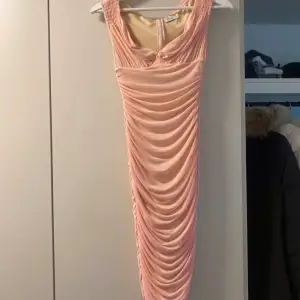 Säljer en superfin rosa sammet klänning med draperad design. Den är ärmlös och har en elegant passform som passar perfekt för festliga tillfällen. Klänningen har en dragkedja i ryggen för enkel påklädning. Perfekt för en glamorös kväll! Använd 1 kväll.