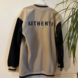 Beige och svart bomberjacka - Säljer en snygg beige och svart bomberjacka. Jackan har långa svarta ärmar och stängs med knappar framtill. Perfekt för höst och vår, och ger en cool och avslappnad stil. Passar både till vardags och fest! Jackan är i mycket bra skick, inga defekter. Storlek M.