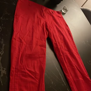 Röda byxor - Snygga röda byxor i en klassisk stil. Perfekta för att liva upp garderoben med en färgklick. De har en enkel design utan synliga detaljer som knappar eller dragkedja, vilket ger dem en stilren look.