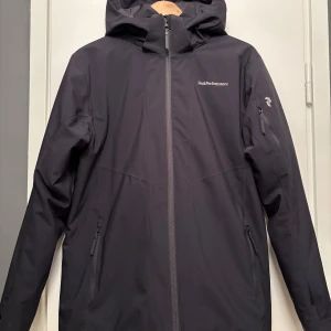 Jacka Peak Performance Jr - Peak Performance modell Jr Maroonj, strlk 170. Mycket fint skick, som ny.  Avtagbar luva, snöskydd i midjan, mjuka resårmuddar i ärmarna.