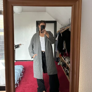 Grå kappa - Tunnare grå kappa i stilig rak passform från danskt klädesmärke. Står strl L men är en perfekt oversized M. Använd av mig några gånger, mycket bra skick på utsidan men några sömmar som har gått upp på insidan. Lätt att laga!