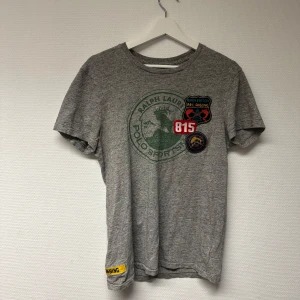 Grå t-shirt från Ralph Lauren - Säljer en skön grå t-shirt från Ralph Lauren med tryck och patchar på framsidan. Dem är i bomull och fett bekväm. Strl: S. Bra skick! 