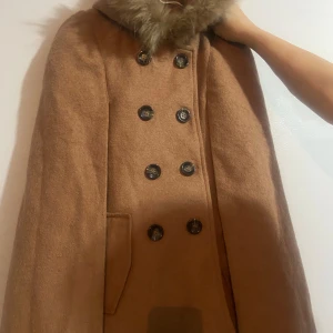 Kappa som sätts på som en cape  - Kappa byggt som en cape, jättte passande till när man vill klä upp sig. Använt 2 gånger och är helt ny. 