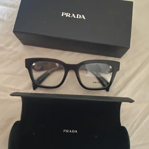Svarta glasögon från Prada - FYND!!! Snygga svarta glasögon från Prada med en klassisk rektangulär form. De har en stilren design med subtila detaljer på bågarna. Perfekta för en elegant och modern look. Aldrig använda satte aldrig i min styrka då jag köpte andra. Nypris 3.400 kr 