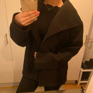 Svart kappa med knappar - Säljer en stilren svart kappa med knappar framtill. Jackan har en klassisk krage och långa ärmar, perfekt för kyligare dagar. ( det är spegeln som är dammig och inte jackan! ) jag köpte den för, 400kr för 1 år sedan💗
