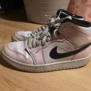 jordan 1s i rosa och svart - Säljer ett par Nike Air sneakers i en snygg kombination av rosa och svart. Skorna har en klassisk design med snörning och perforerade detaljer på tån. Perfekta för en sportig look.