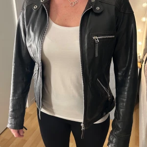 Svart skinnjacka från Alvaro by Hollies - Snygg svart skinnjacka från Alvaro by Hollies med dragkedja och flera fickor. Jackan har en klassisk design med långa ärmar och en stilren look. Perfekt för att ge din outfit en edgy touch.💞