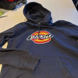 Mörkblå hoodie från Dickies - Säljer en snygg mörkblå hoodie från Dickies med det klassiska logotyptrycket på bröstet. Hoodien har en stor ficka framtill och justerbar huva med dragsko. Perfekt för en avslappnad stil.