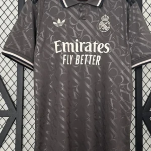 Grå fotbollströja från Adidas - Snygg grå fotbollströja från Adidas med Real Madrid-logga och 'Emirates Fly Better' tryckt på framsidan. Tröjan har korta ärmar med vita detaljer och ett diskret mönster över hela tyget. Perfekt för fotbollsfans som vill visa sitt stöd med stil.