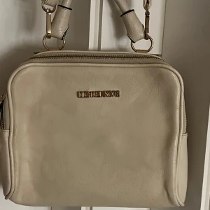 Beige axelväska från Michael Kors - Snygg beige axelväska från Michael Kors i skinn. Väskan har en praktisk dragkedja och justerbar axelrem. Perfekt för att bära dina dagliga nödvändigheter med stil.