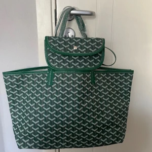 Grön mönstrad väska - Snygg grön shoppingväska med ett fint mönster. Väskan har två handtag och en matchande avtagbar liten väska med knappstängning. Köpt för 900kr på en secondhand affär i Spaninen, aldrig använt och har inga defekter❤️Perfekt för att bära med sig allt man behöver under dagen. Säljer samma i grå också! Kan gå ner i pris vid snabb affär!