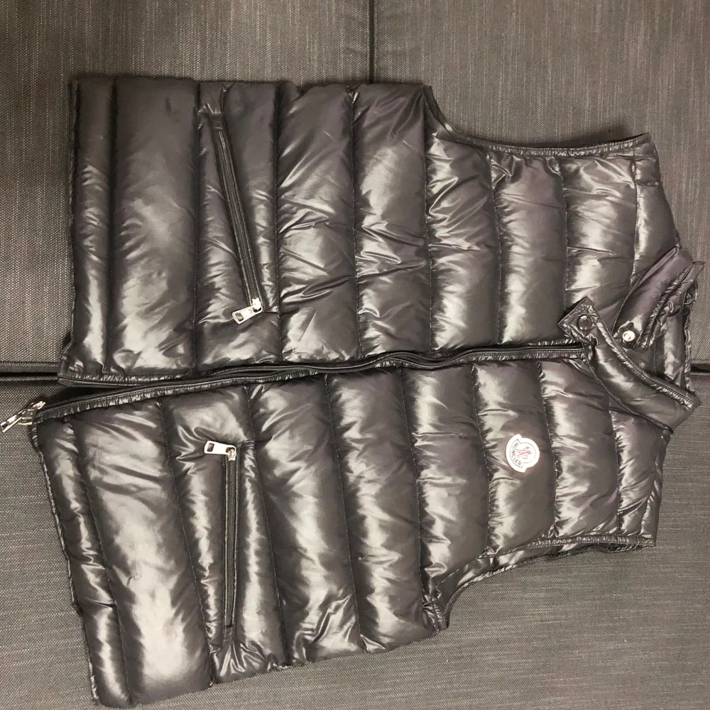 Snygg svart dunväst från Moncler med dragkedja och två praktiska fickor framtill. Perfekt för kyligare dagar när du vill hålla stilen. Västen har en klassisk design med Moncler-logga på bröstet. Och priset går att diskutera . Takit.