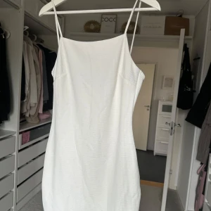 Vit ribbad klänning - Säljer en stilren vit ribbad klänning med smala axelband. Perfekt för en somrig look. Klänningen har en enkel och elegant design som passar till många tillfällen.