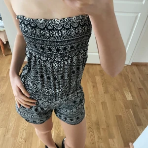 Svartvit axelbandslös jumpsuit - Snygg och bekväm axelbandslös jumpsuit i svartvitt mönster. Perfekt för varma sommardagar med sin lätta och luftiga design. Den har en elastisk överdel för bra passform och korta ben.