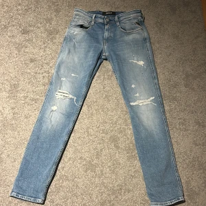 Blå jeans från Replay - Snygga ljusblå jeans från Replay, modell Anbass. De har en straight passform med slitna detaljer och en klassisk passform. Jeansen är helt oanvända och köpta för 1600 på jeansbolaget.