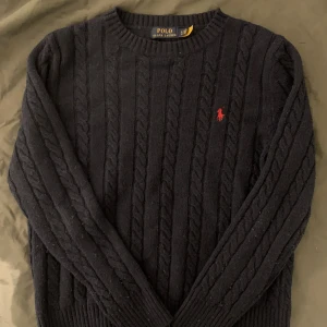 Mörkblå kabelstickad tröja från Ralph Lauren - Säljer en stilren marinblå kabelstickad tröja från Ralph Lauren med det klassiska röda logotypen på bröstet. Tröjan har långa ärmar och ribbstickade muddar vid ärmslut och nederkant. Perfekt för kyligare dagar! Xl i barn storlek, pris kan diskuteras 