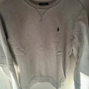Grå sweatshirt från Ralph Lauren - Säljer en klassisk grå sweatshirt från Ralph Lauren med det ikoniska logotypbroderiet på bröstet. Tröjan har rund hals och långa ärmar, perfekt för en avslappnad stil. Passar bra till både jeans och chinos.