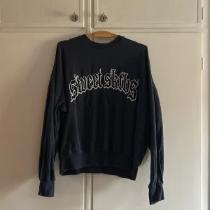 Svart sweatshirt från Sweet SKTBS - Säljer en mörkblå sweatshirt från Sweet SKTBS med tryck i gotisk stil på framsidan. Tröjan har långa ärmar och en klassisk rund halsringning. Perfekt för en avslappnad stil.