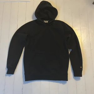 Svart hoodie från Carhartt - Säljer en klassisk svart hoodie från Carhartt. Den har en rymlig huva och en stor magficka framtill. Passar även S
