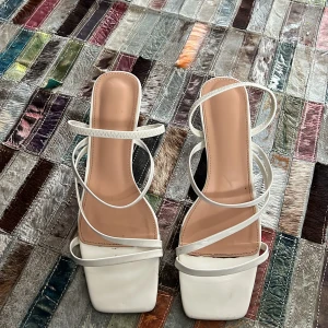 Vita sandaler med klack - Eleganta vita sandaler med smala remmar och fyrkantig tå. De har en stilren design med en liten klack som ger en sofistikerad look. Perfekta för sommarens alla tillfällen.