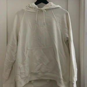Vit hoodie från H&M - Säljer en stilren vit hoodie från H&M Basics. Den är aldrig använd men prislappen sitter inte kvar. Har en ficka och justerbar luva.