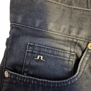 Svarta jeans från J.Lindeberg - Snygga svarta jeans från J.Lindeberg med klassisk femficksdesign och knappgylf. Perfekta för en stilren look. Märkeslogga på den lilla fickan och insidan av midjan. 32/32 strl