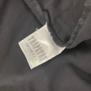 Svart t-shirt från Trapstar - Snygg svart t-shirt från Trapstar med ett coolt broderat märke i orange och grått på framsidan. Perfekt för att ge din outfit en edgy touch.