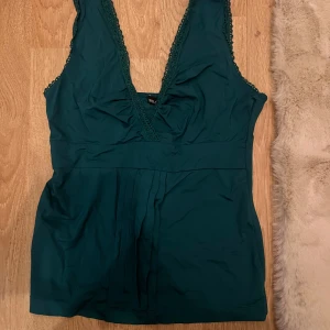 Mörkgrön spetsdetaljerad topp från mango - Mörkgrön ärmlös topp med djup v-ringning och spetsdetaljer längs kanterna från mango. Storlek S men passar även M eftersom den är stretchy. 