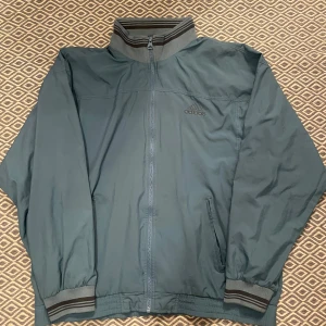 Gråblå vindjacka från Adidas - Vind/vårjacka från adidas. Köpt på Vinted men är i väldigt bra skick! Storlek L, med en baggy fit. KÖP ENDAST VIA POSTNORD