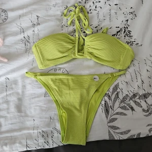 Grön bikini från Hunkemöller - Snygg grön bikini från Hunkemöller i storlek S. Överdelen har knytband och en ribbad textur som ger en trendig look. Perfekt för sommarens stranddagar!