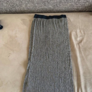 Glittrig kjol från Gina Tricot - Snygg glittrig kjol från Gina Tricot i en elegant silverfärg. Kjolen har en elastisk midja för bekväm passform och ett stilrent plisserat mönster. Perfekt för att lägga till lite glamour i garderoben.