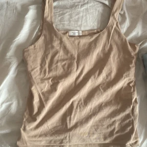 Beige linnetopp från Gina Tricot - Säljer en enkel och stilren beige linnetopp från Gina Tricot. Perfekt för varma dagar eller som lager under andra plagg. Toppen har en klassisk design med breda axelband.