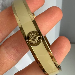 Guldarmband från Dyrberg/Kern - Elegant guldarmband med en stilren design. Armbandet har en slät yta och en diskret logotyp ingraverad på framsidan. Perfekt för att ge en lyxig touch till din outfit.